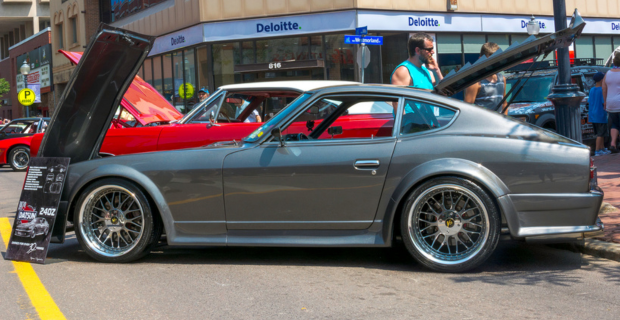 A dark grey 1970 Nissan Datsun 240Z at a car show with the hood up. 