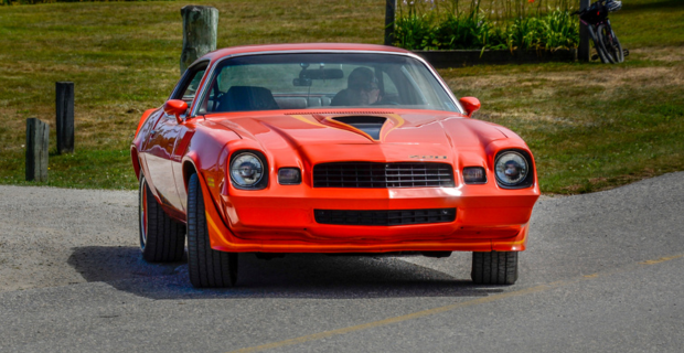 An orange 1980 Chevy Camaro turning on a country road.